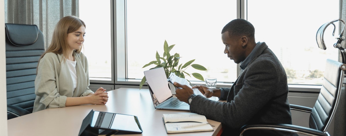 A man and woman sit across a desk from one another during a job interview.