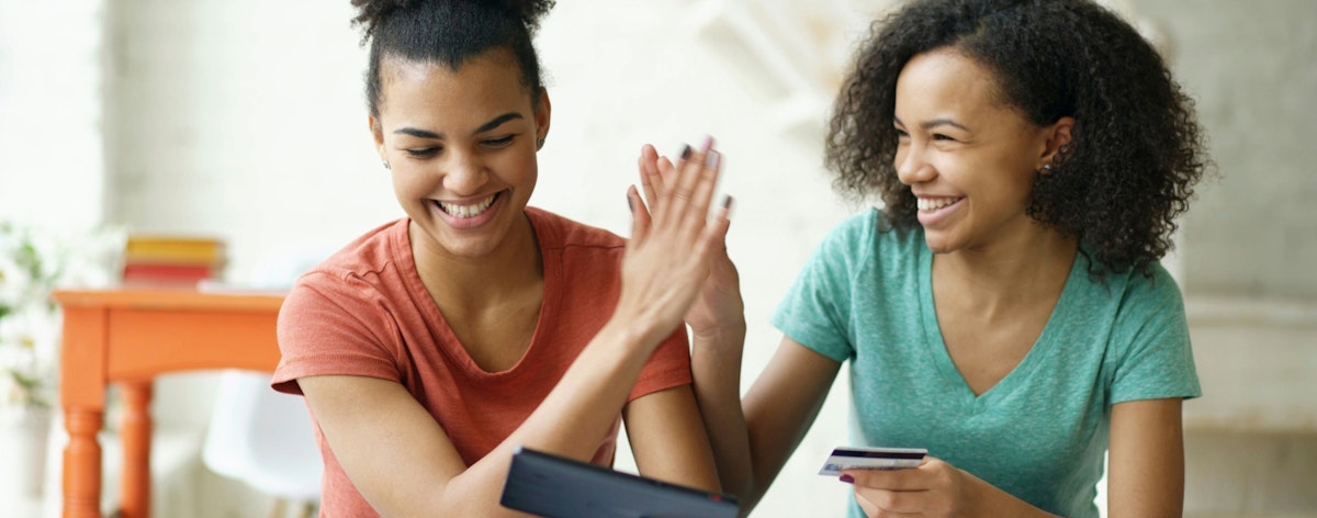 Two girls high five while holding a credit card.