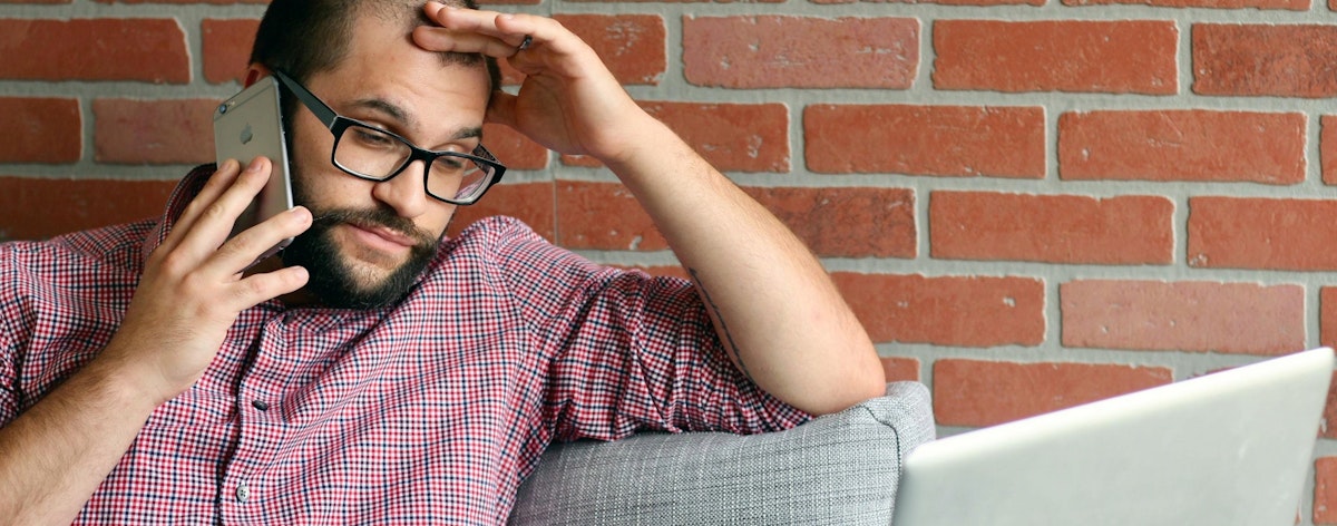 A man looks stressed as he talks on the phone and looks at his computer
