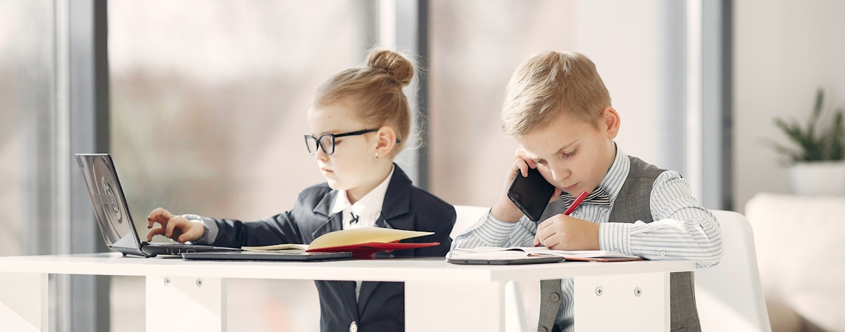 Two kids dressed in suits work at a desk.
